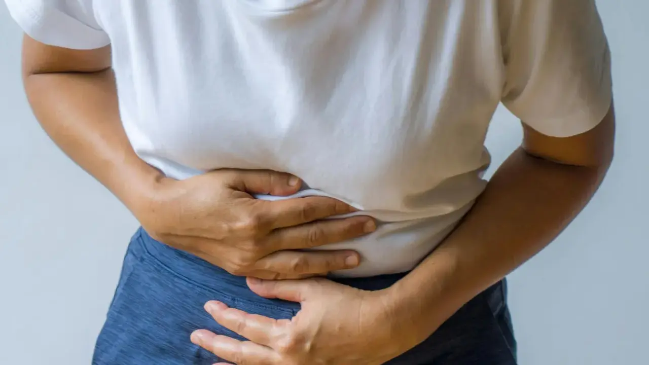 Person håller sig om magen, upplever smärta som kan vara relaterad till IBS och ont i ryggen.