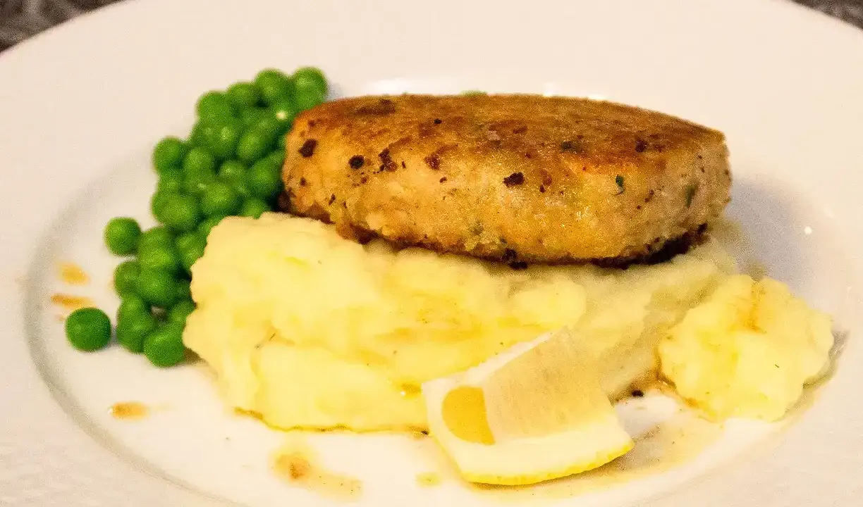 En gyllene havets wallenbergare serveras med krämigt potatismos, gröna ärtor och en citronskiva.