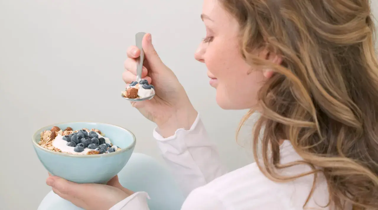 En kvinna äter en skål med yoghurt, blåbär och nötter. En hälsosam frukost som kan hjälpa till att få ner blodsockret.