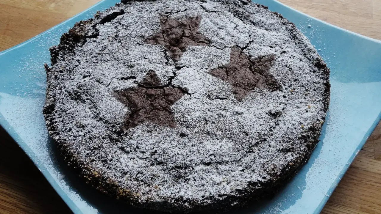 En härlig glutenfri kladdkaka med stjärnmönster av florsocker på en blå tallrik.
