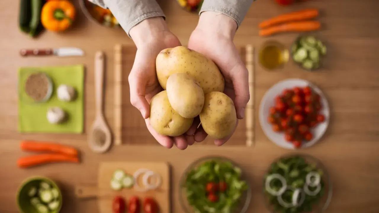 Händer håller färsk potatis, en del av en hälsosam måltid med grönsaker. Potatis nyttigt!