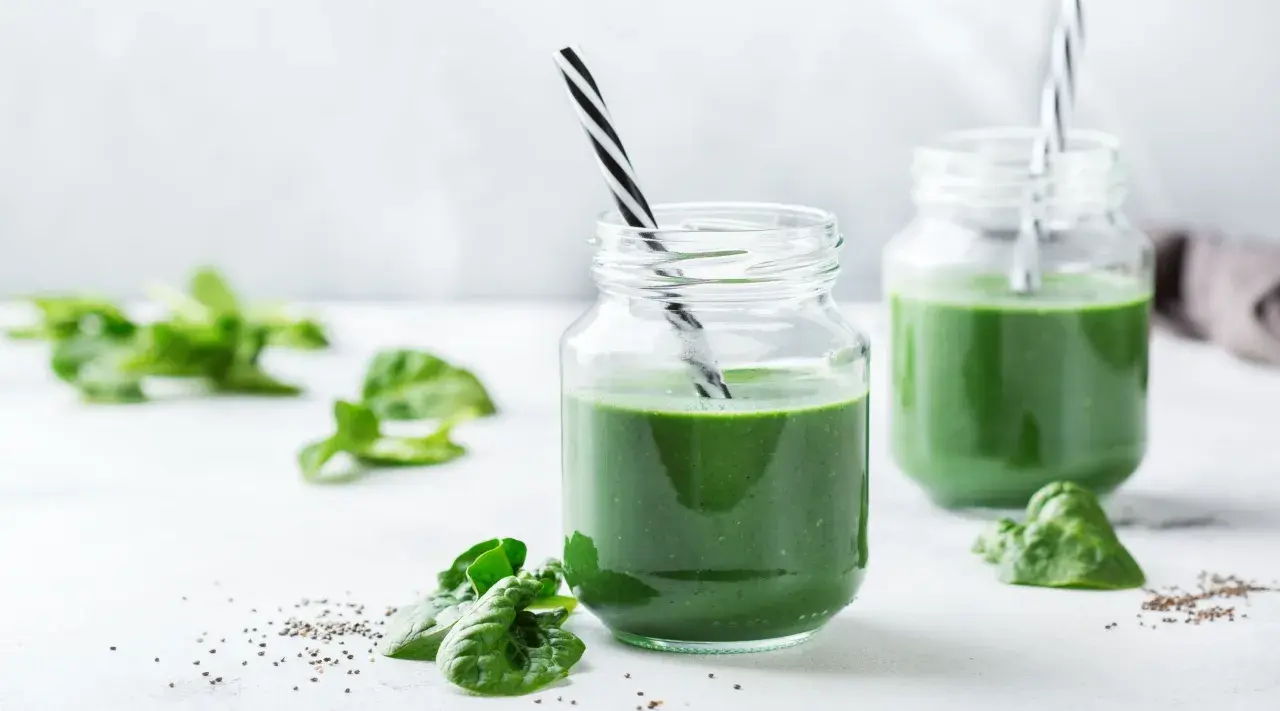 Två glas med grön smoothie, garnerade med färsk spenat och chiafrön. Tänk på spirulina biverkningar innan du dricker för mycket.
