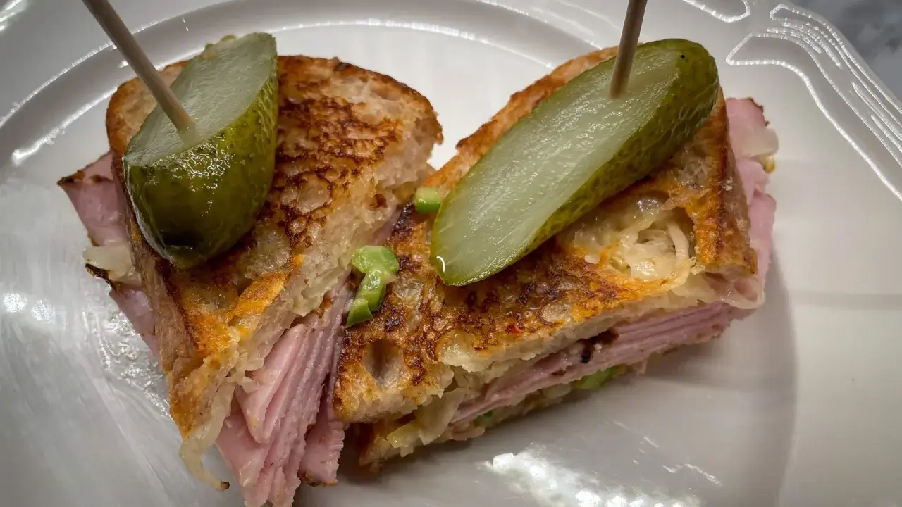 En saftig reuben sandwich med skinka, surkål och rostat bröd, toppad med dillgurka.
