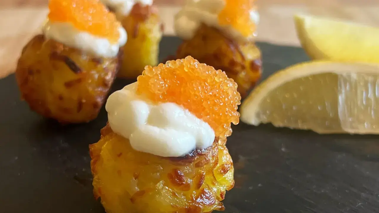 Små, krispiga tater tots toppade med gräddfil och orange rom. Citronklyftor ligger bredvid.