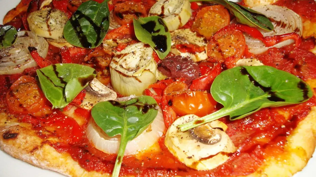 En läcker glutenfri pizza med tomatsås, grönsaker som lök, paprika, champinjoner, kronärtskocka och färsk spenat, toppad med balsamvinäger.