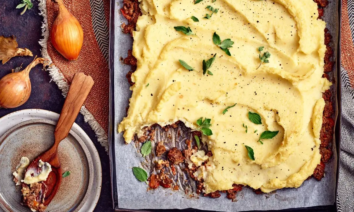 En ugnsbakad köttfärspaj med ett fluffigt potatismos som täcker hela ytan. Serveras med färska örter och peppar.