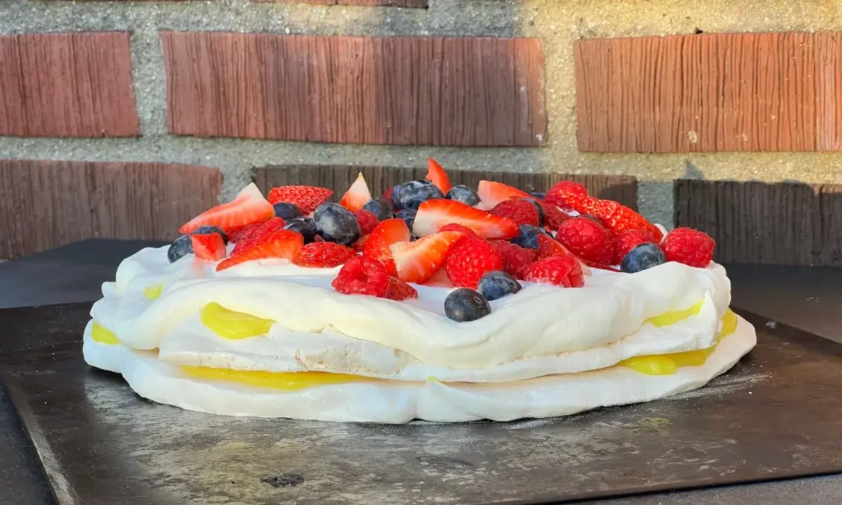 En vacker pavlova med lemoncurd, toppad med färska bär som jordgubbar, hallon och blåbär.