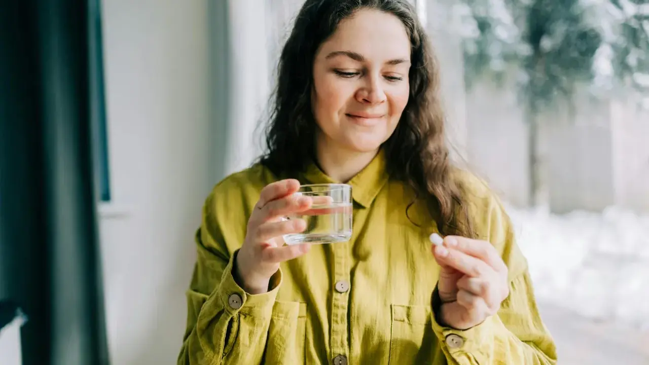 Kvinna med glas vatten och en tablett, funderar på magnesium tillskott biverkningar.