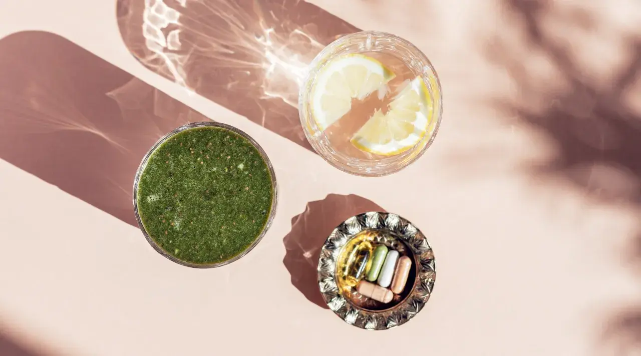 Grön smoothie, citronvatten och kapslar med spårämnen i en vacker ljusmiljö.