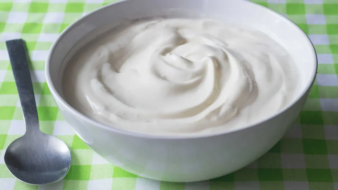 En skål med krämig yoghurt, redo att avnjutas. En sked ligger bredvid, perfekt för att ta en tugga av denna e 407-godhet.