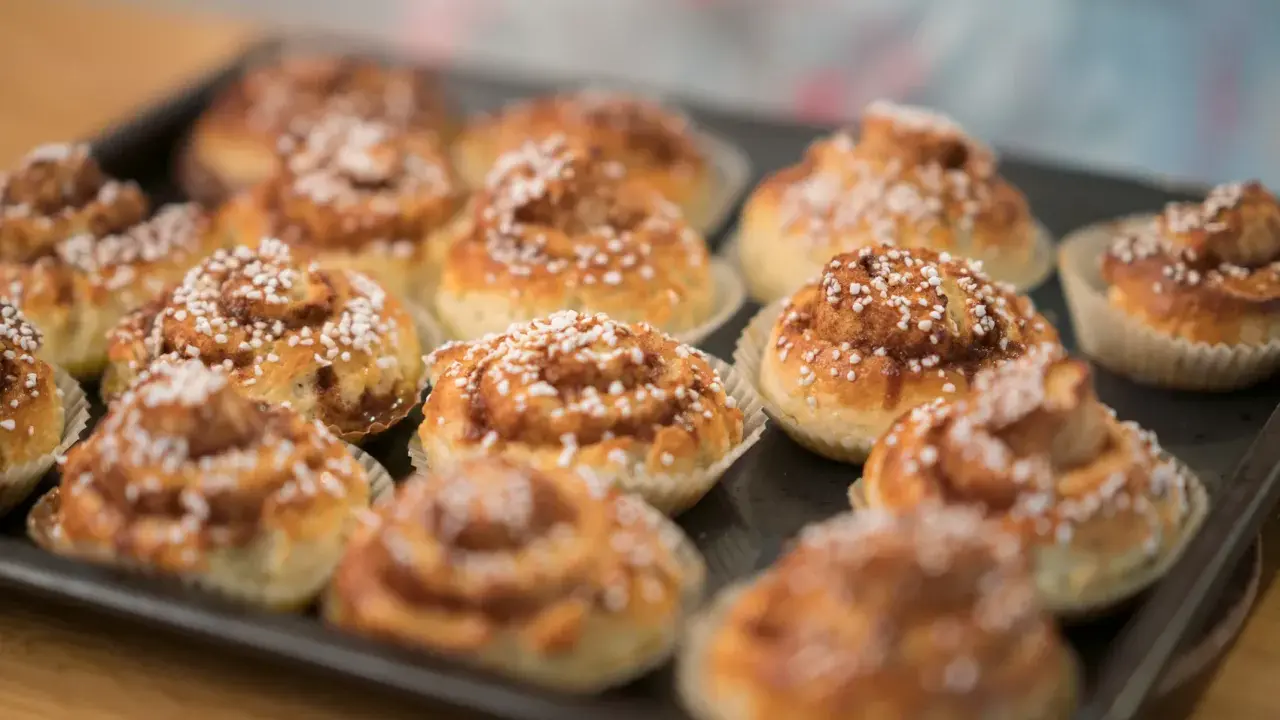 En plåt med nybakade glutenfria kanelbullar, toppade med pärlsocker. Doften av kanel sprider sig i köket.