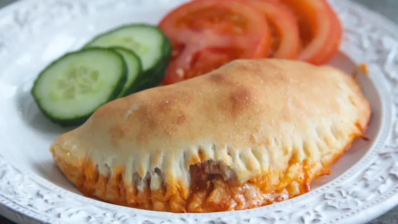 En gyllene pirog med ost och tomatsås, serverad med skivor av tomat och gurka. Ett perfekt piroger recept för en snabb och god måltid.