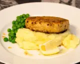 En gyllene havets wallenbergare serveras med krämigt potatismos, gröna ärtor och en citronskiva.