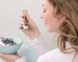 En kvinna äter en skål med yoghurt, blåbär och nötter. En hälsosam frukost som kan hjälpa till att få ner blodsockret.