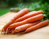 En hög med färska, orange morötter med gröna blastar ligger på en träskärbräda. Dessa nyttiga rotfrukter, som finns i morot, är redo att användas i köket.