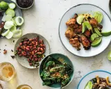 En härlig dukning med olika rätter av thai mat: kycklingvingar, friterade gröna paprikor, jordnötter och omogna mangos.
