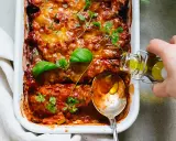 En ugnsbakad auberginegratäng med tomatsås och ost, toppad med färska örter. En sked och en flaska olivolja antyder ett läckert aubergine recept.