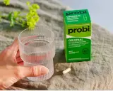 En hand håller ett glas vatten bredvid en förpackning med probi. En kapsel ligger på bordet, redo att tas för att undvika probi mage biverkningar.