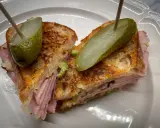 En saftig reuben sandwich med skinka, surkål och rostat bröd, toppad med dillgurka.