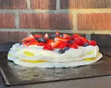 En vacker pavlova med lemoncurd, toppad med färska bär som jordgubbar, hallon och blåbär.
