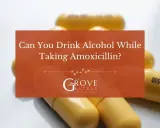 Gula kapslar med texten "AMOX 500" ligger utspridda. En orange ruta frågar: "Can You Drink Alcohol While Taking Amoxicillin?".