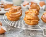 Gyllene petit choux på ett vitt galler, med äggskal och ägg i bakgrunden.
