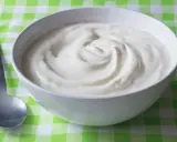 En skål med krämig yoghurt, redo att avnjutas. En sked ligger bredvid, perfekt för att ta en tugga av denna e 407-godhet.