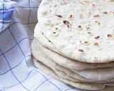 En hög med nybakade tortillas, perfekta för ditt nästa tortilla recept. En blårutig kökshandduk ligger bredvid.