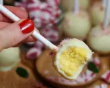 En hand med rött nagellack håller en cake pop. Den är doppad i vit choklad och strössel.