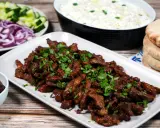 En tallrik med saftigt gyroskött, toppat med färsk persilja. Bredvid syns pitabröd, tzatziki, oliver, gurka och rödlök. Ett perfekt gyros recept!