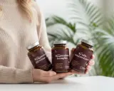Person håller tre burkar med magnesiumtillskott. Frågan "hur många mg magnesium per dag" kan besvaras med hjälp av informationen på burkarna.