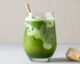 Grönt matcha te med mjölk och is i ett glas, med en bambuvisp bredvid. Tänk på eventuella matcha te biverkningar innan du dricker.