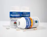 Tre burkar kosttillskott med magnesium. En burk ligger ner och visar texten "Magnesiumtaurat", som bidrar till att minska trötthet och utmattning, vilket är viktigt för magnesium i kroppen.