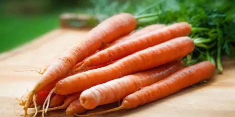 En hög med färska, orange morötter med gröna blastar ligger på en träskärbräda. Dessa nyttiga rotfrukter, som finns i morot, är redo att användas i köket.