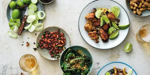 En härlig dukning med olika rätter av thai mat: kycklingvingar, friterade gröna paprikor, jordnötter och omogna mangos.