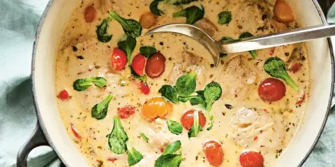 En krämig provensalsk kycklinggryta med körsbärstomater och gröna blad i en gjutjärnsgryta.