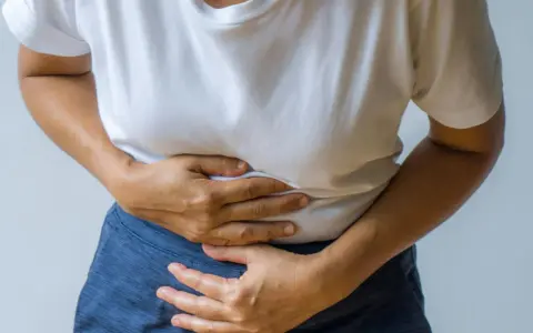 Person håller sig om magen, upplever smärta som kan vara relaterad till IBS och ont i ryggen.