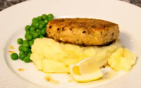 En gyllene havets wallenbergare serveras med krämigt potatismos, gröna ärtor och en citronskiva.