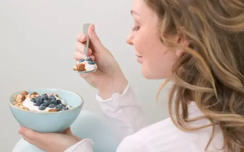 En kvinna äter en skål med yoghurt, blåbär och nötter. En hälsosam frukost som kan hjälpa till att få ner blodsockret.