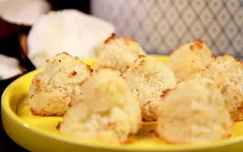 Små, gyllene kokostoppar på en gul tallrik, redo att avnjutas. Ett enkelt kokostoppar recept för hembakning.