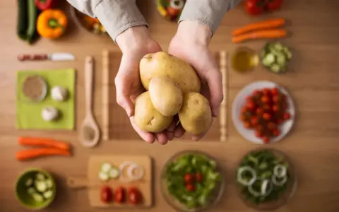 Händer håller färsk potatis, en del av en hälsosam måltid med grönsaker. Potatis nyttigt!