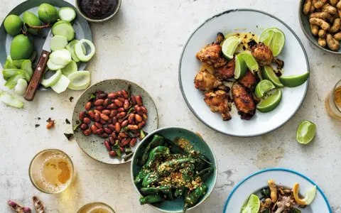 En härlig dukning med olika rätter av thai mat: kycklingvingar, friterade gröna paprikor, jordnötter och omogna mangos.