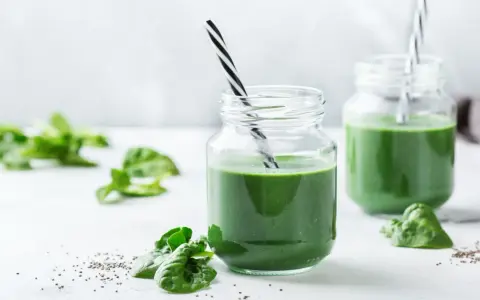 Två glas med grön smoothie, garnerade med färsk spenat och chiafrön. Tänk på spirulina biverkningar innan du dricker för mycket.