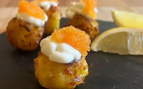 Små, krispiga tater tots toppade med gräddfil och orange rom. Citronklyftor ligger bredvid.