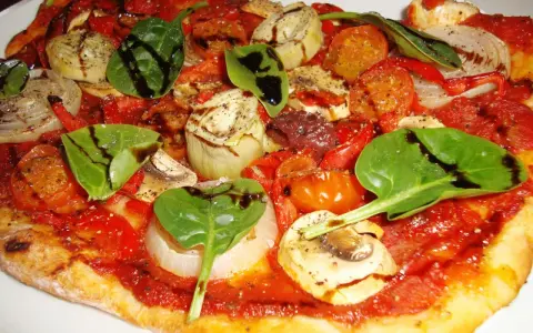 En läcker glutenfri pizza med tomatsås, grönsaker som lök, paprika, champinjoner, kronärtskocka och färsk spenat, toppad med balsamvinäger.