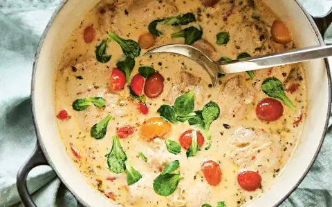 En krämig provensalsk kycklinggryta med körsbärstomater och gröna blad i en gjutjärnsgryta.