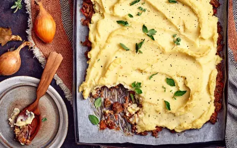 En ugnsbakad köttfärspaj med ett fluffigt potatismos som täcker hela ytan. Serveras med färska örter och peppar.