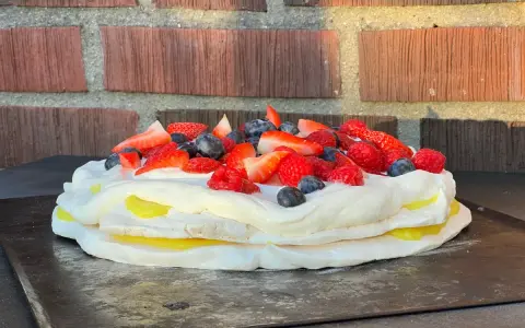 En vacker pavlova med lemoncurd, toppad med färska bär som jordgubbar, hallon och blåbär.