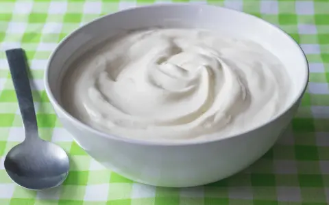 En skål med krämig yoghurt, redo att avnjutas. En sked ligger bredvid, perfekt för att ta en tugga av denna e 407-godhet.
