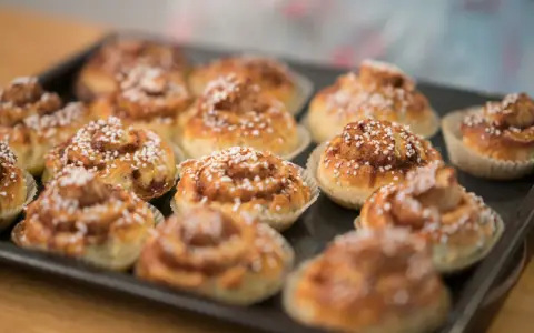 En plåt med nybakade glutenfria kanelbullar, toppade med pärlsocker. Doften av kanel sprider sig i köket.